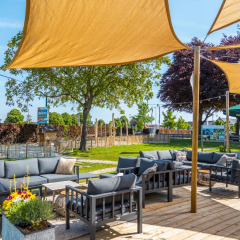 Gemütlicher Loungebereich im Freien mit Sofas und Sonnensegel in einem Glamping-Ferienpark.