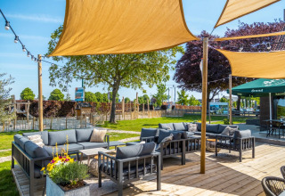 Zona de descanso al aire libre con sofás y toldos de sombra en un parque vacacional con glamping.