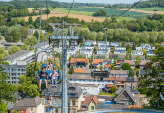 Mensen in een stoeltjeslift over een vakantiepark met glamping, uitkijkend over huizen en groene velden.