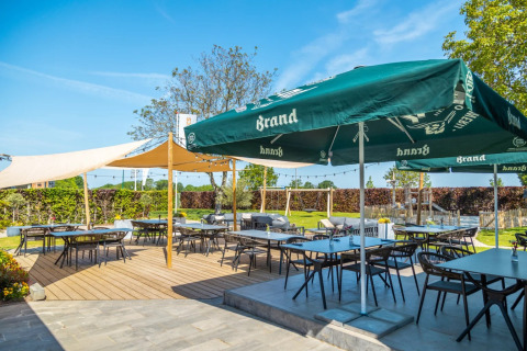 Zona exterior de comedor en un parque vacacional de glamping, mesas bajo sombrillas verdes y césped.