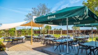 Außenterrasse eines Ferienparks mit Glamping, Tischen unter großen Sonnenschirmen und viel Grün.