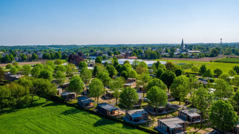 Vista aérea de un parque vacacional con alojamientos glamping, rodeado de árboles verdes y paisajes rurales.