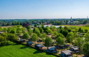 Luchtfoto van een vakantiepark met glampinghutten, omgeven door groene natuur en open velden.