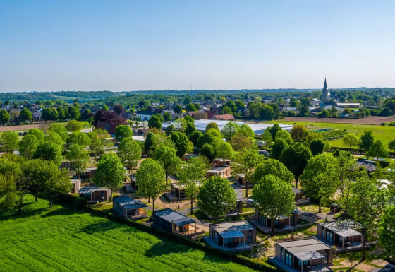 Luftfoto af feriepark med glamping-hytter, grønne træer og marker i et fredeligt landskab.