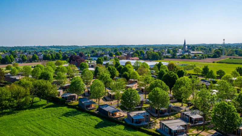 Luchtfoto van een vakantiepark met glamping-accommodaties, omgeven door groene bomen en weilanden.