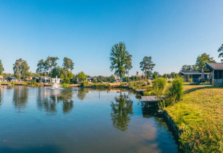 Panoramisch uitzicht op een vakantiepark met luxe glamping-accommodaties aan een rustige plas en blauwe lucht.