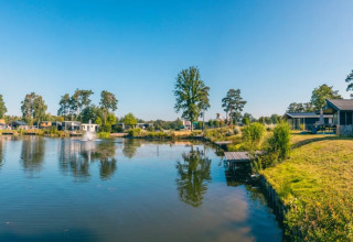Panoramabillede af et feriepark med luksushytter og søudsigt under en klar blå himmel.