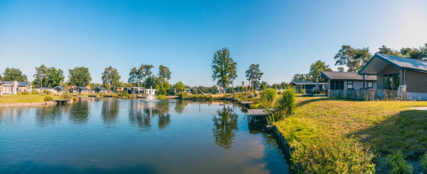 Panoramabillede af et feriepark med luksushytter og søudsigt under en klar blå himmel.