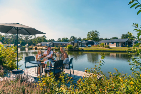 Familia disfruta de una comida al aire libre junto al lago en un parque con alojamientos glamping modernos.