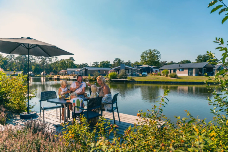 Familie speist draußen am See in einem Ferienpark mit Glamping-Unterkünften und modernen Bungalows.