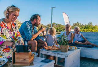 Familia disfruta de una comida al aire libre con pizza en un parque vacacional de glamping bajo cielo azul.