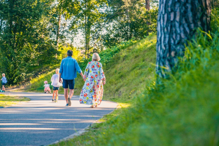 Familie spaziert Hand in Hand auf einem Weg im Ferienpark mit Glamping, umgeben von Bäumen und Wiese.