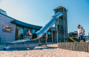Kinderen spelen op een grote glijbaan met zand bij een vakantiepark met glamping op een zonnige dag.