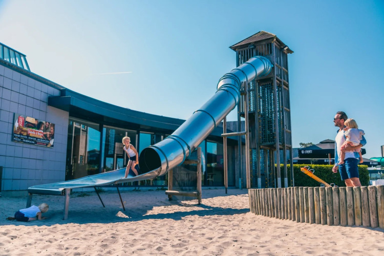 Kinder spielen auf einer Riesenrutsche mit Sand bei einem Ferienpark mit Glamping-Angeboten an einem sonnigen Tag.