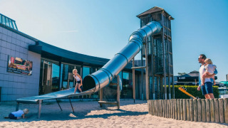 Kinder spielen auf einer Riesenrutsche mit Sand bei einem Ferienpark mit Glamping-Angeboten an einem sonnigen Tag.
