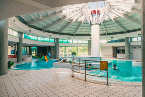 Innenpool in einem Ferienpark mit Glamping, Rutsche und Kindern beim Spielen unter einer großen Kuppel.