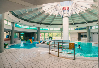 Indendørs swimmingpool i en feriepark med glamping, rutsjebaner og legende børn under et stort kuppelloft.