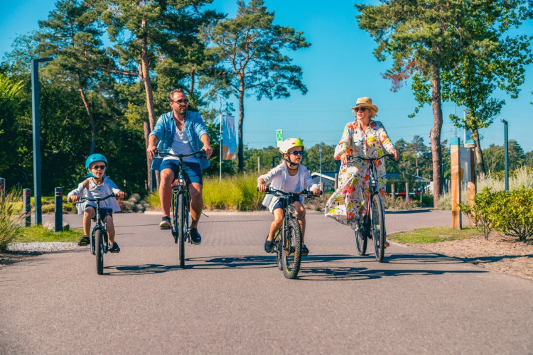Une famille fait du vélo lors d’une journée ensoleillée dans un parc de vacances avec hébergements glamping.