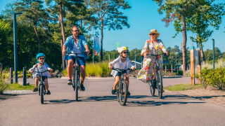 Eine Familie fährt an einem sonnigen Tag in einem Ferienpark mit Glamping-Angeboten und Natur Rad.