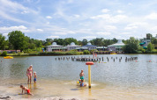 Gezinnen amuseren zich aan het strand van een vakantiepark met glamping, kinderen spelen in het water.