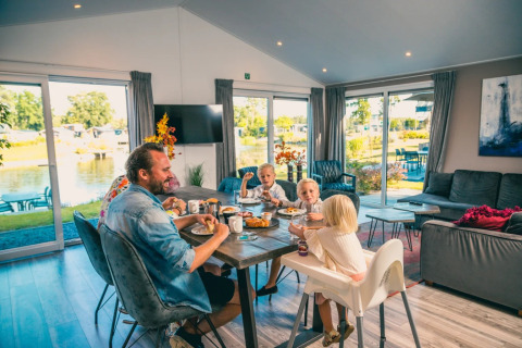 Famille prenant le petit-déjeuner dans un lodge glamping avec grandes fenêtres sur un lac de vacances.