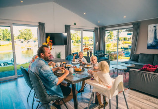 Gezin aan het ontbijten in een glamping lodge met uitzicht op een vijver in een vakantiepark.