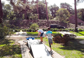 Deux garçons jouent au mini-golf dans un parc de vacances entouré de verdure et d'hébergements glamping.