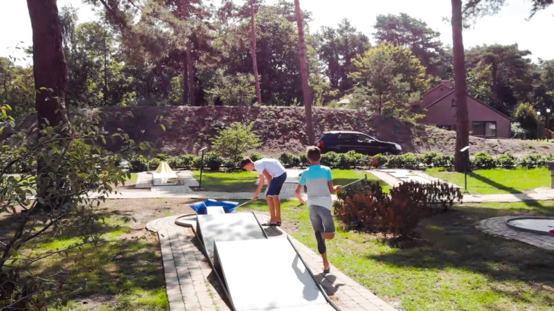 Zwei Jungen spielen Minigolf in einem Ferienpark mit Glamping-Angeboten und viel Natur im Hintergrund.