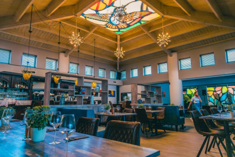 Schickes Restaurant in einem Glamping-Park mit buntem Glasdach, moderner Einrichtung und Pflanzen am Tisch.