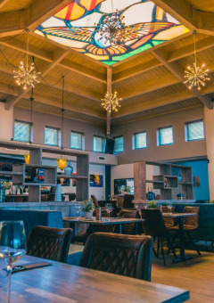 Schickes Restaurant in einem Glamping-Park mit buntem Glasdach, moderner Einrichtung und Pflanzen am Tisch.