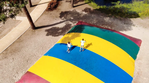 Zwei Kinder spielen auf einem großen, bunten Luftkissen in einem Glamping-Ferienpark im Freien.