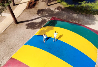 Two kids playing on a large colorful jumping pillow at an outdoor holiday park with glamping options.