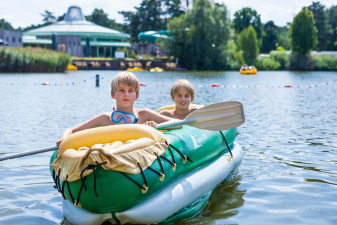 Twee kinderen varen in een groene opblaasboot op het meer van een vakantiedomein met glamping.