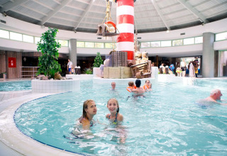 Piscine intérieure dans un parc de vacances glamping, enfants et adultes près d’un phare coloré.