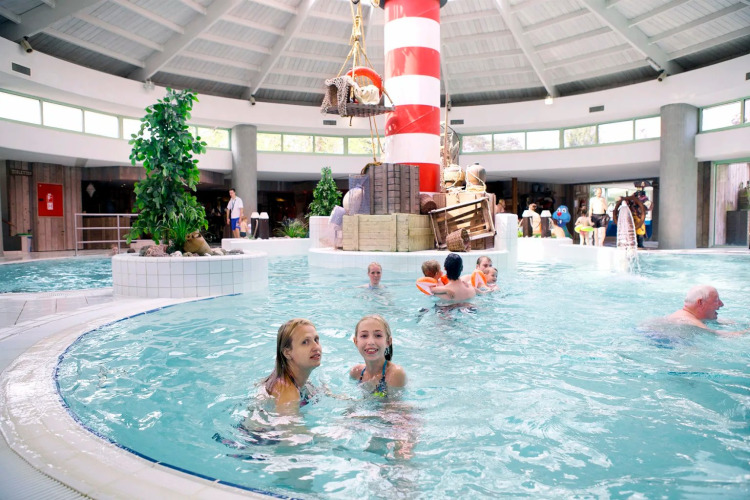 Innenpool in einem Ferienpark mit Glamping, Kinder und Erwachsene schwimmen nahe einem Leuchtturm.