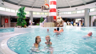 Innenpool in einem Ferienpark mit Glamping, Kinder und Erwachsene schwimmen nahe einem Leuchtturm.