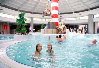 Innenpool in einem Ferienpark mit Glamping, Kinder und Erwachsene schwimmen nahe einem Leuchtturm.