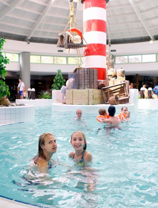 Indoor swimming pool at a holiday park with glamping, kids and adults enjoying water near a lighthouse.