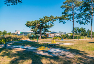 Buiten minigolfbaan bij een vakantiepark met glamping, omgeven door bomen en moderne gebouwen op de achtergrond.