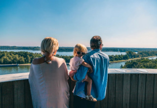 Familie nyder udsigten over en flod fra en feriepark med glamping, solskin og grønne omgivelser.