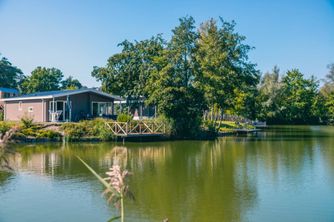 Ferienpark mit Glamping-Unterkünften am See, umgeben von Bäumen und Natur, unter blauem Himmel.