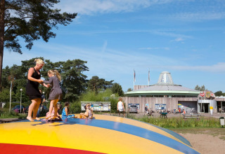Des adultes et enfants s'amusent sur une structure gonflable dans un parc de vacances entouré d’arbres.