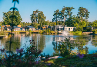 Moderne Glamping-Hütten am See mit Springbrunnen, umgeben von Bäumen in einem Ferienpark.