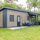 Moderne skovlodge med træfacade og udendørs siddeplads ved Kampeerdorp de Zandstuve i Holland.