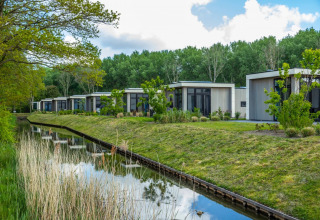 Cabañas glamping modernas junto a un canal rodeado de vegetación en un tranquilo parque vacacional.