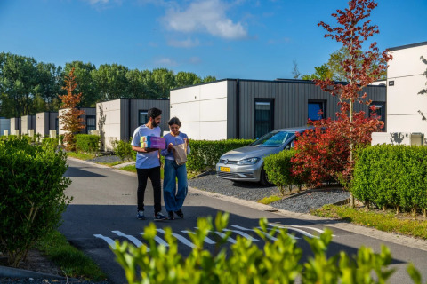 Una giovane coppia passeggia in un villaggio vacanze con sistemazioni glamping moderne circondate dal verde.