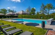 Udendørs swimmingpool i et feriepark med liggestole, parasoller og grønne omgivelser under en blå himmel.