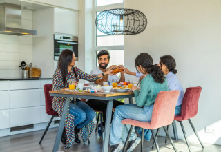 Gezin aan het ontbijten aan een tafel in de keuken van een moderne glampingaccommodatie in een vakantiepark.