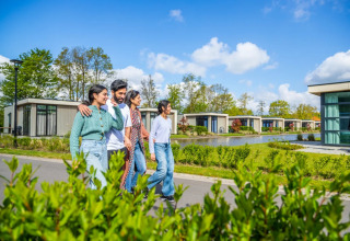 A group of people walking happily past modern glamping lodges by a pond at a holiday park resort.