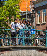 Un grupo de jóvenes disfruta de un día soleado sobre un puente con bicicletas en una ciudad holandesa pintoresca.